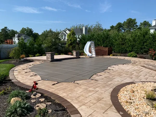 Tan LOOP-LOC mesh safety cover over a curved pool with a stone deck